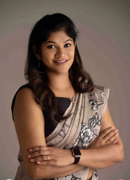 Picture5 | Dr Swetha Cosmodermcentre Portrait of a smiling woman with dark hair, wearing a beige floral saree over a black blouse, arms crossed and a smartwatch on her left wrist.
